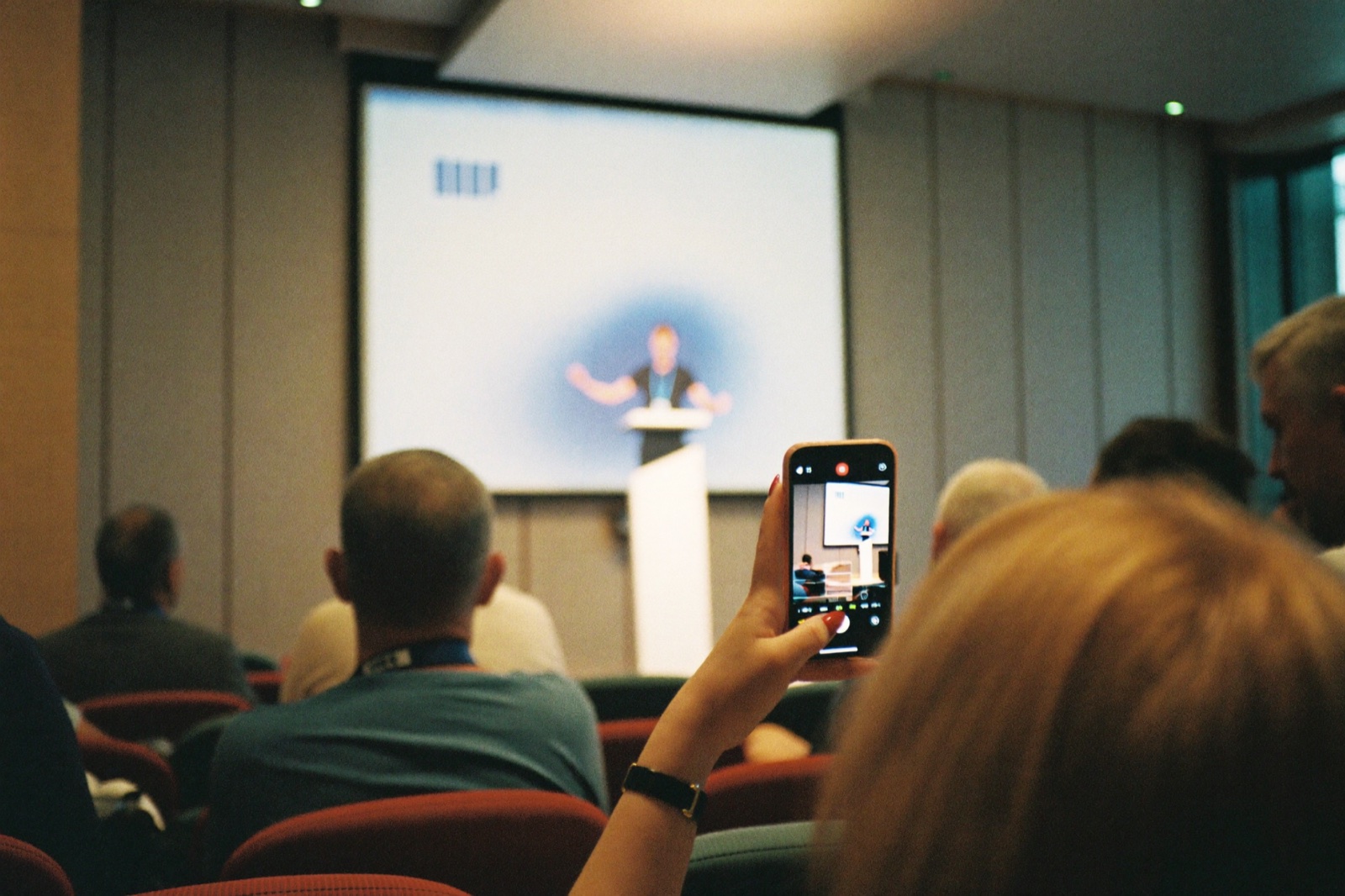 Účastníčka konferencie natáča rečníka na iPhone